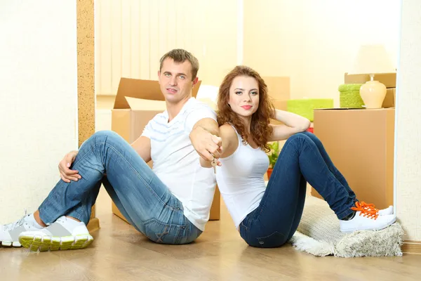 Pareja joven con las llaves de su nuevo hogar en el fondo de la habitación — Foto de Stock