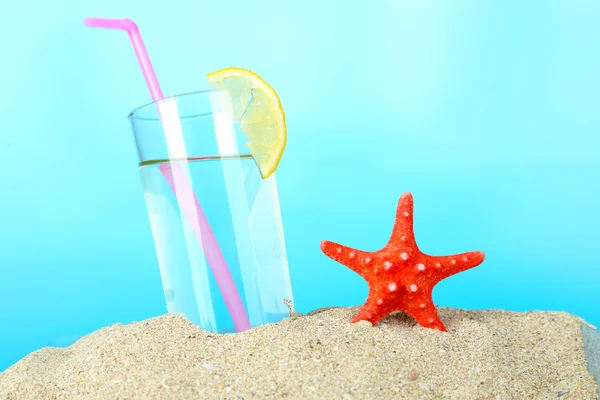 Beach cocktail in sand on blue background — Stock Photo, Image