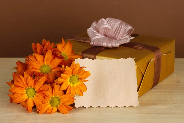 Boş etiket ve kahverengi zemin üzerine masaya çiçek hediye kutusu — Stok fotoğraf