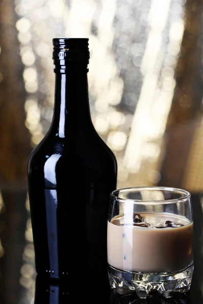 Baileys liqueur in bottle and glass on golden background — Stock Photo, Image