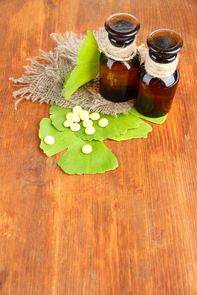 Ginkgo biloba foglie e bottiglie di medicina su sfondo di legno — Foto Stock