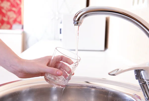 Hand holding glass of water poured from kitchen faucet — Stock Photo, Image