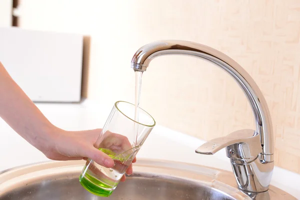 Hand holding glass of water poured from kitchen faucet — Stock Photo, Image