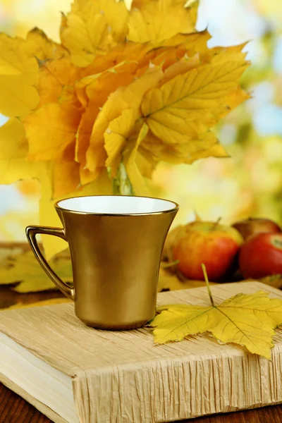 Folhas de outono, xícara e livro em mesa de madeira sobre fundo natural — Fotografia de Stock