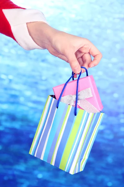 Hand holds package with New Year gift on blue background