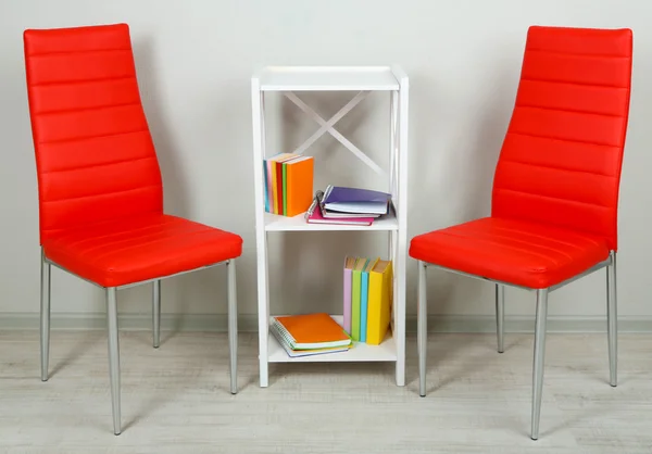 Schönes Interieur mit modernen Farbstühlen, Büchern auf Holzständer, auf Wandhintergrund — Stockfoto