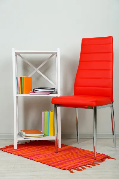 Hermoso interior con silla de color moderno, libros sobre soporte de madera, sobre fondo de pared —  Fotos de Stock