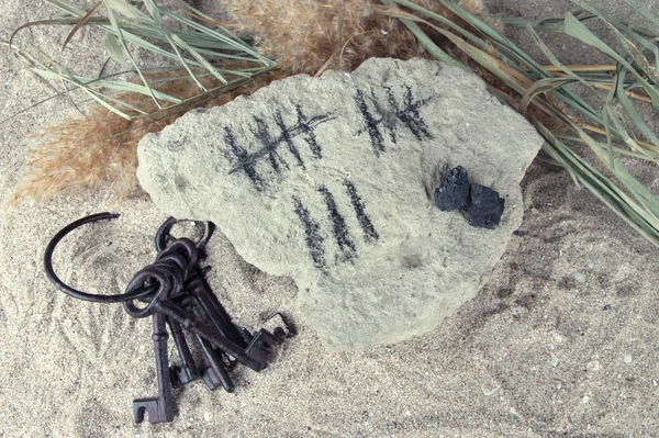 砂の背景のキーを持つ石の上にスティックを描くことによって日を数える — ストック写真