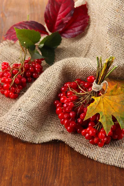 Red berries of viburnum on sackcloth napkin, on wooden background — Stock Photo, Image