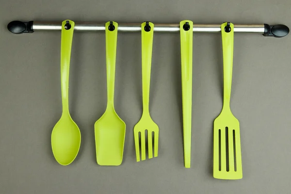Plastic kitchen utensils on silver hooks on grey background — Stock Photo, Image