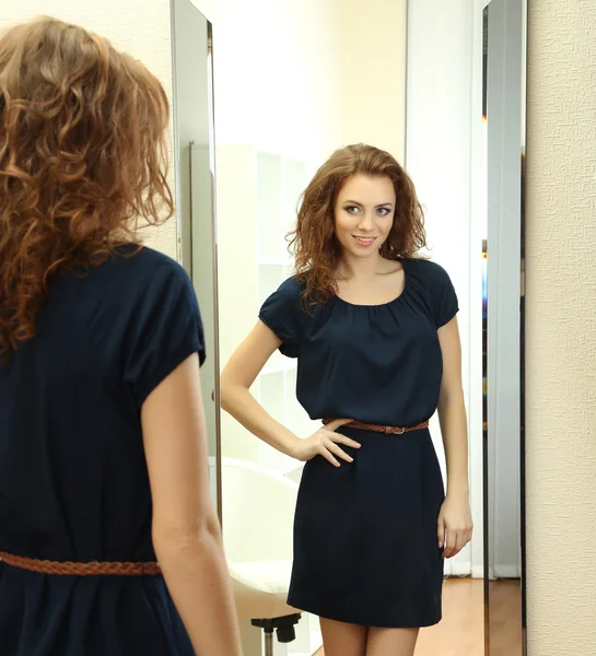 Hermosa chica tratando de vestir cerca del espejo en la habitación —  Fotos de Stock