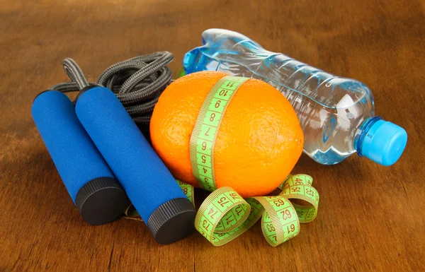 Orange with measuring tape, skipping rope and bottle of water, on wooden background — стоковое фото