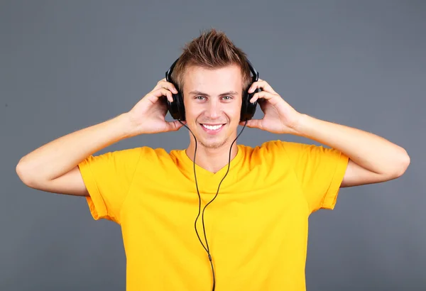 Yakışıklı genç adam gri arka planda müzik dinlemek — Stok fotoğraf