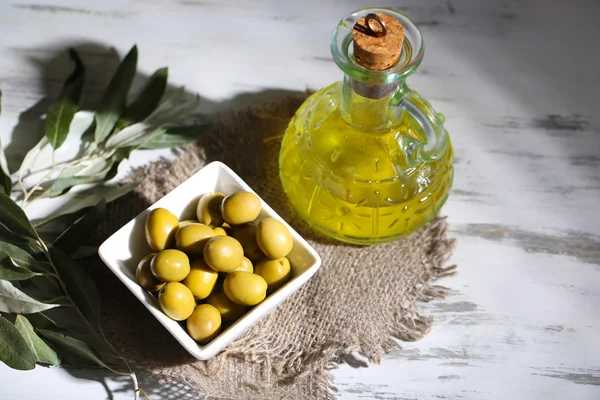 Olio e olive in ciotola su sacco su tavola di legno — Foto Stock