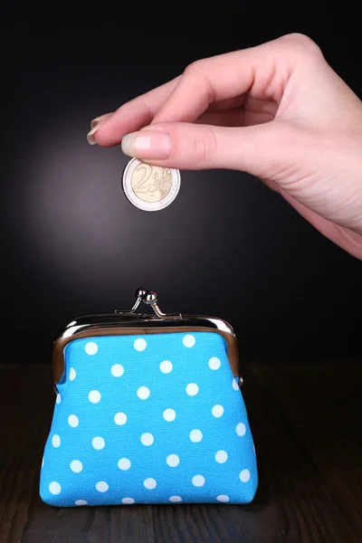 Blue purse and coin in female hand on table on black background — Stock Photo, Image