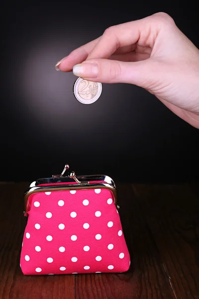 Pink purse and coin in female hand on table on black background — Stock Photo, Image