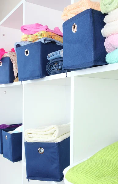 Blue textile boxes with towels and clothes in white shelves — Stock Photo, Image