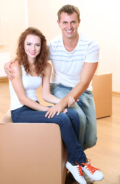 Young couple with boxes in new home on room background — Stock Photo, Image