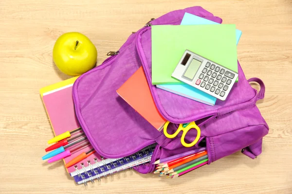 Purple backpack with school supplies on wooden background — Stock Photo, Image