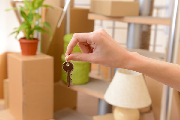 Female hand with keys ob stack of cartons background: moving house concept