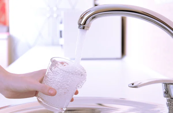 Hand som håller glas vatten hälls från köksblandare — Stockfoto