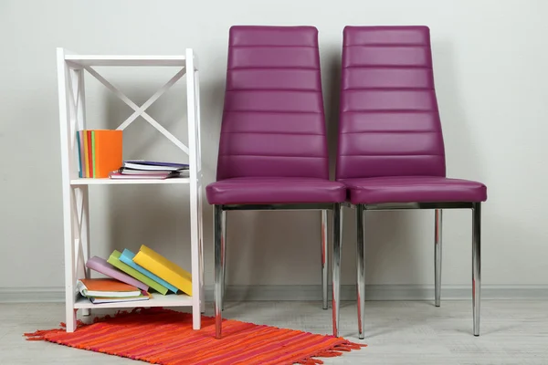 Bel intérieur avec des chaises de couleur modernes, livres sur support en bois, sur fond mural — Photo