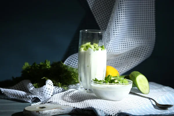 Cam ve tahta masada koyu arka plan üzerinde renkli peçete üzerinde kase yoğurt salatalık — Stok fotoğraf