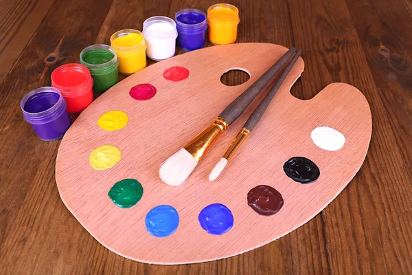 Wooden art palette with paint and brushes on table close-up — Stock Photo, Image