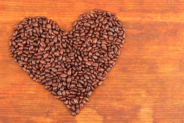 Сердце подсолнечника зерна в шоколаде, на коричневом деревянном фоне — стоковое фото