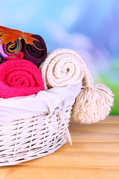 Warm knitted scarves in basket on wooden table on natural background — Stock Photo, Image