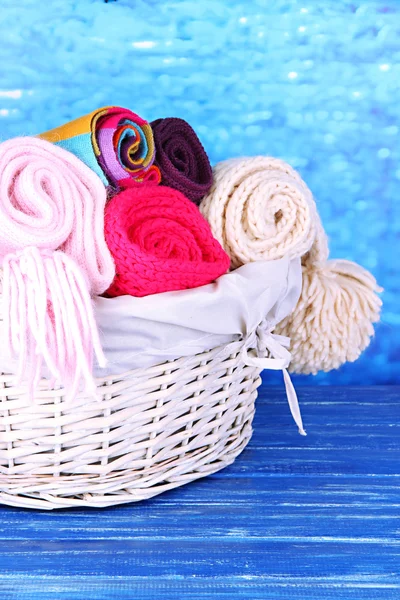 Warm knitted scarves in basket on wooden table on blue background — Stock Photo, Image
