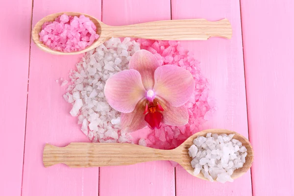 Натюрморт с красивым цветущим цветком орхидеи и деревянные ложки с морской солью, на цветном деревянном фоне — стоковое фото