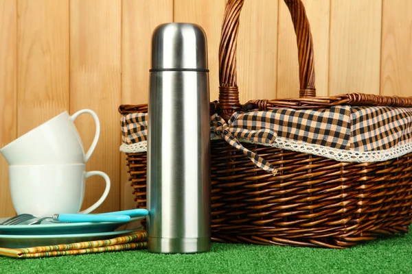 Thermos avec tasses, assiettes et panier sur herbe — Photo