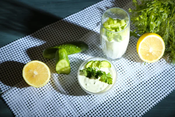 Gurkenjoghurt in Glas und Schüssel, auf Farbserviette, auf Holzbrett, auf dunklem Hintergrund — Stockfoto