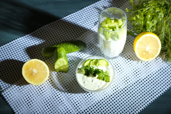 Yogur de pepino en vidrio y tazón, sobre servilleta de color, sobre tabla de madera, sobre fondo oscuro —  Fotos de Stock