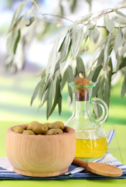 Olive oil and olives in bowl on napkin on wooden table on nature background — Stock Photo, Image