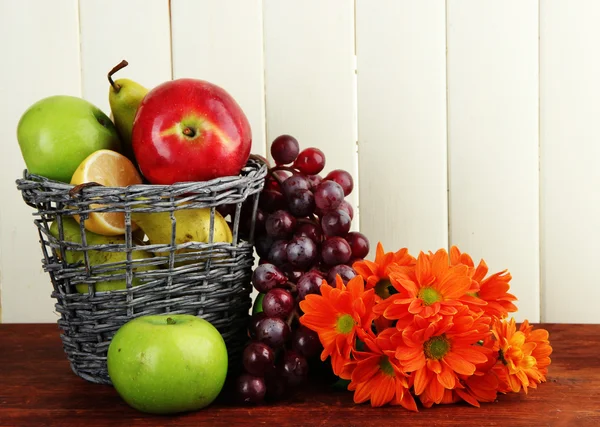 Diferentes frutas en cesta y flores en mesa —  Fotos de Stock