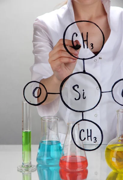 Chemist woman writing formulas on glass on grey background — Stock Photo, Image