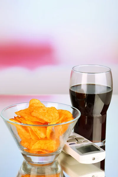 Chips en tazón, cola y control remoto de TV sobre fondo brillante — Foto de Stock