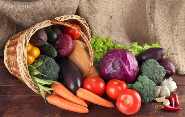 Forskellige grøntsager i kurv på bordet på sækkeklud baggrund - Stock-foto