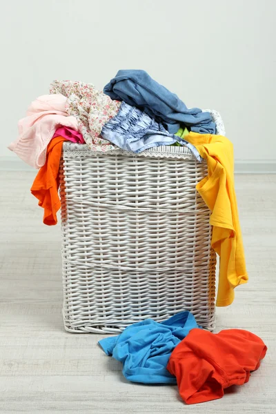 Full laundry basket on wooden floor on gray background — Stock Photo, Image