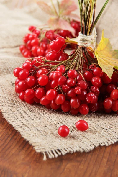 Red berries of viburnum on sackcloth napkin, on wooden background — Stock Photo, Image