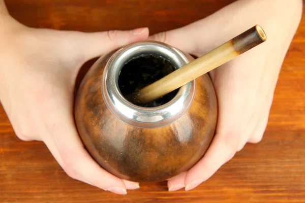 Manos de mujer sosteniendo calabaza y bombilla con yerba mate sobre fondo de madera —  Fotos de Stock