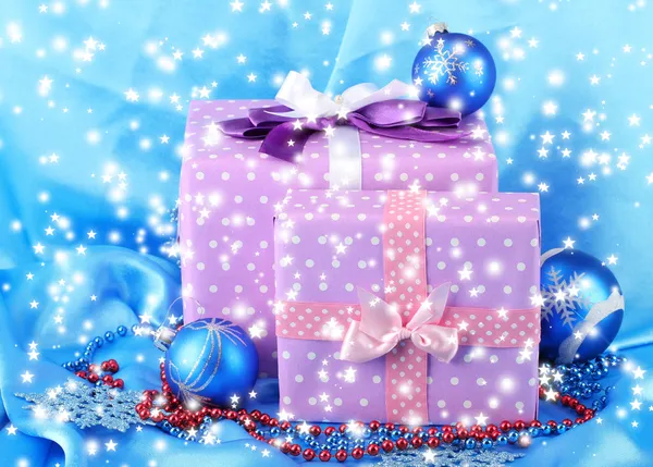 Beautiful purple in peas gifts with blue Christmas balls, snowflakes and beads on blue background — Stock Photo, Image