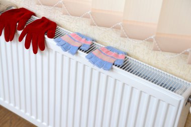 Knitted gloves drying on heating radiator clipart