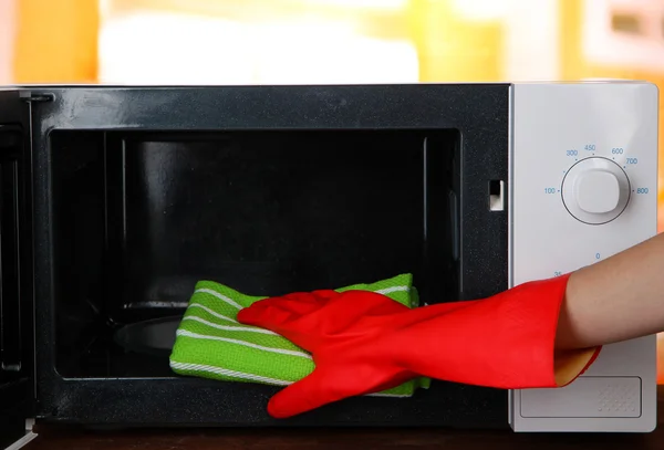 Χέρι με microfiber καθαρισμού φούρνο μικροκυμάτων, σε φωτεινό φόντο — Φωτογραφία Αρχείου