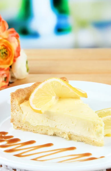 Scheibe Zitronenkäsekuchen mit Soße auf Teller, auf Holztisch, auf hellem Hintergrund — Stockfoto