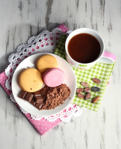 Kakao im Becher mit Süßigkeiten und Kakaopulver auf Teller auf Holztisch — Stockfoto