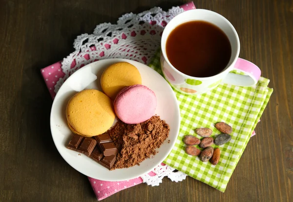 Kakao im Becher mit Süßigkeiten und Kakaopulver auf Teller auf Holztisch — Stockfoto