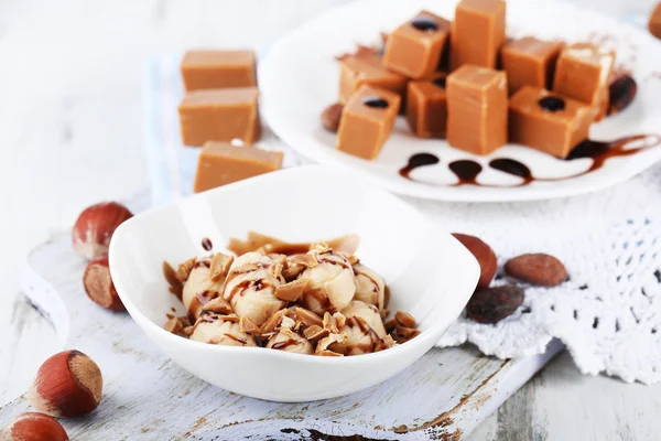 Many toffee on plate and in bowl on napkin on board on wooden table — Stock Photo, Image